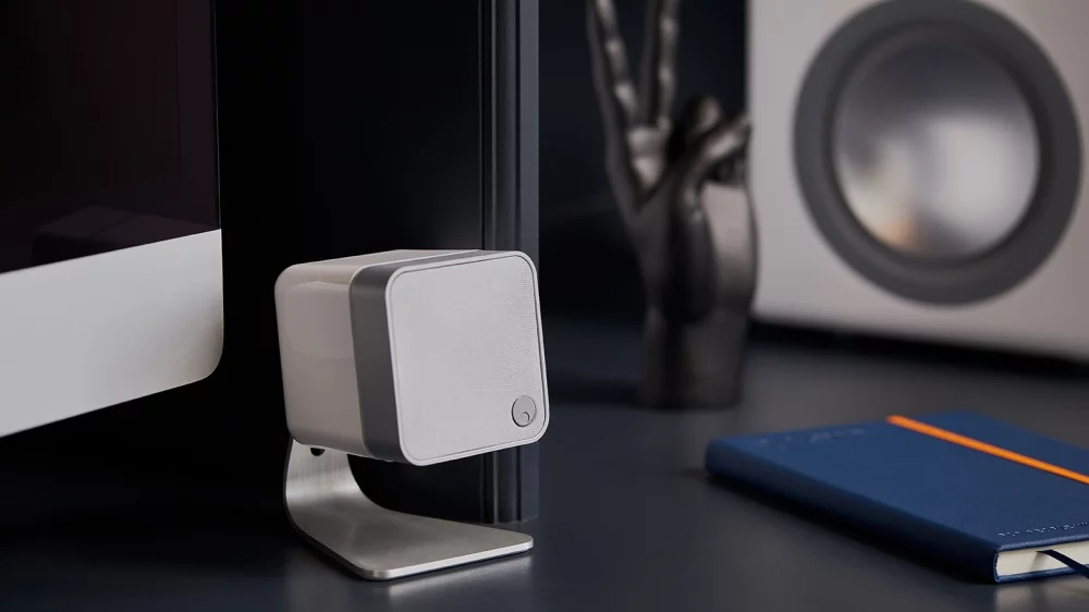 white minx min 12 speaker on table stand, stood on desk with computer and blue notebook