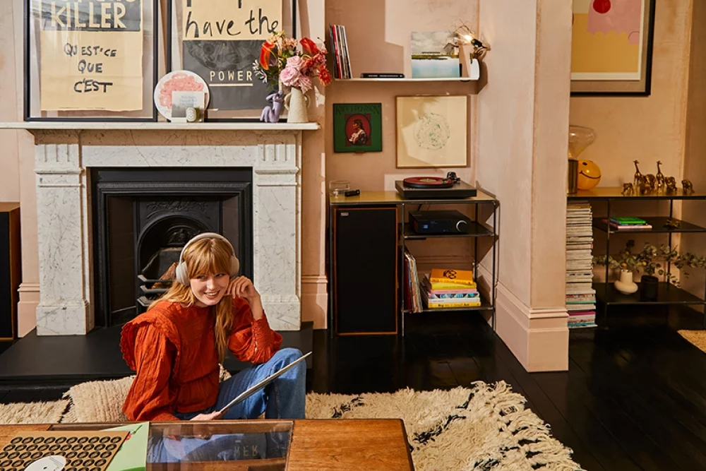 Woman wearing headphones sat on living room floor choosing records